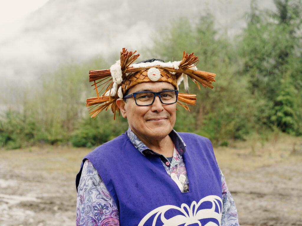 Chief John Powell smiles, wearing purple regalia, with mist and trees in the background at Mamalilikulla's recently declared Indigenous protected area