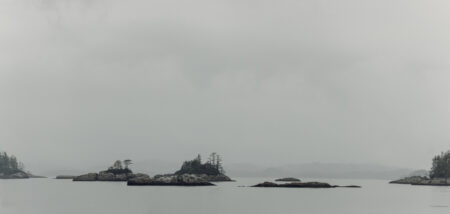 Mamalilikulla territory a ide landscape shot of grey water and grey sky meeting in the distance, and rocks and small islands with trees sit in the water.