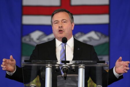 Jason Kenney stands in front of a large Alberta flag.