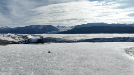Researchers studying the Milne Ice Shelf in an expansive arctic landscape with mountains in the background.