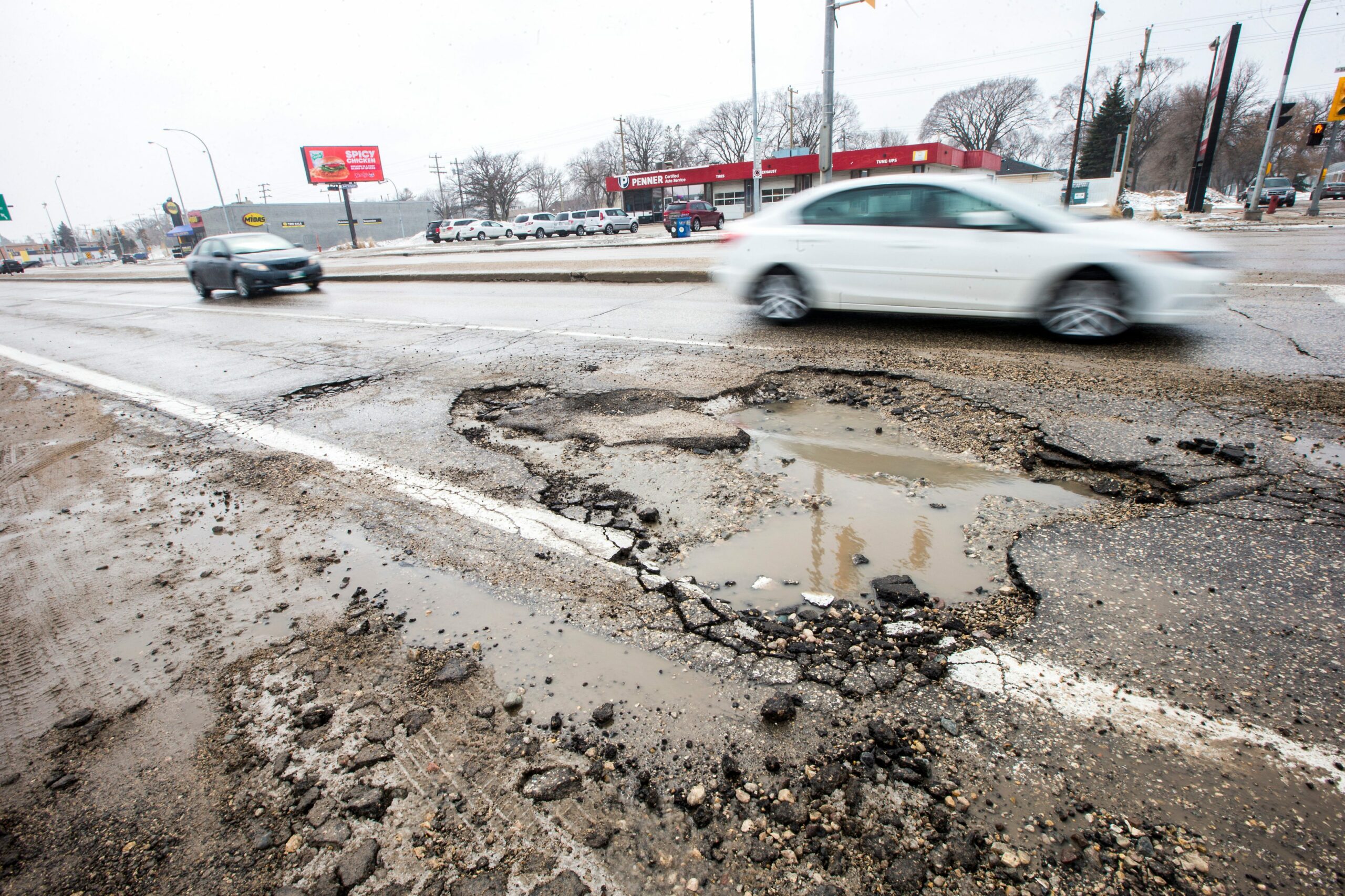 Cars in motion drive past a large water filled pothole on a Winnipeg street