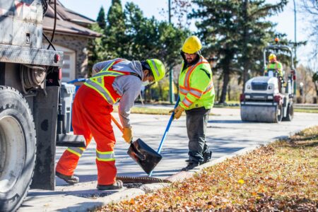 City employees in reflective construction gear fill and rake asphalt through a pothole on a Winnipeg street