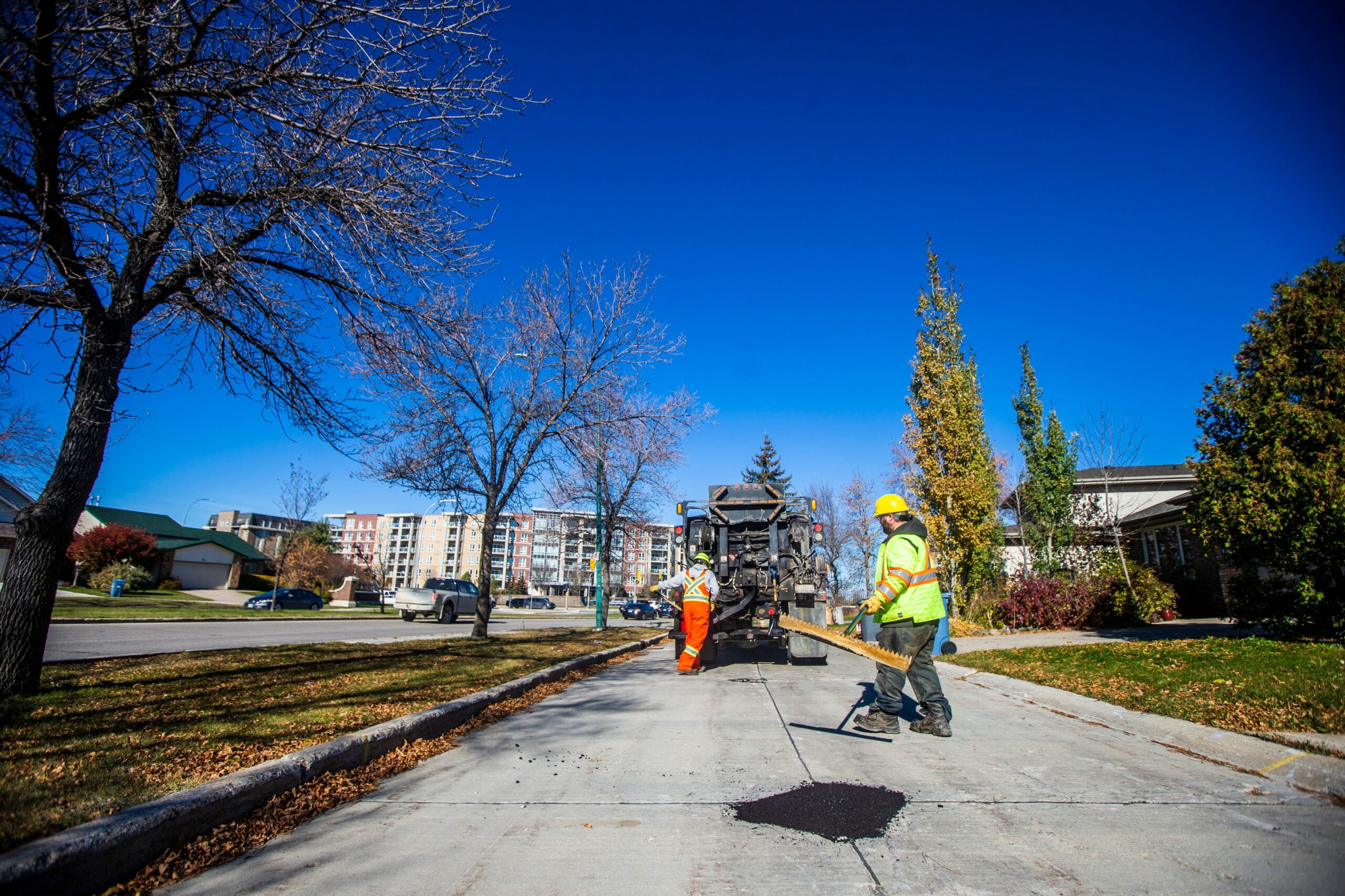 A group of city crew staff in reflective work gear move down the street after filling a pothole in the foreground