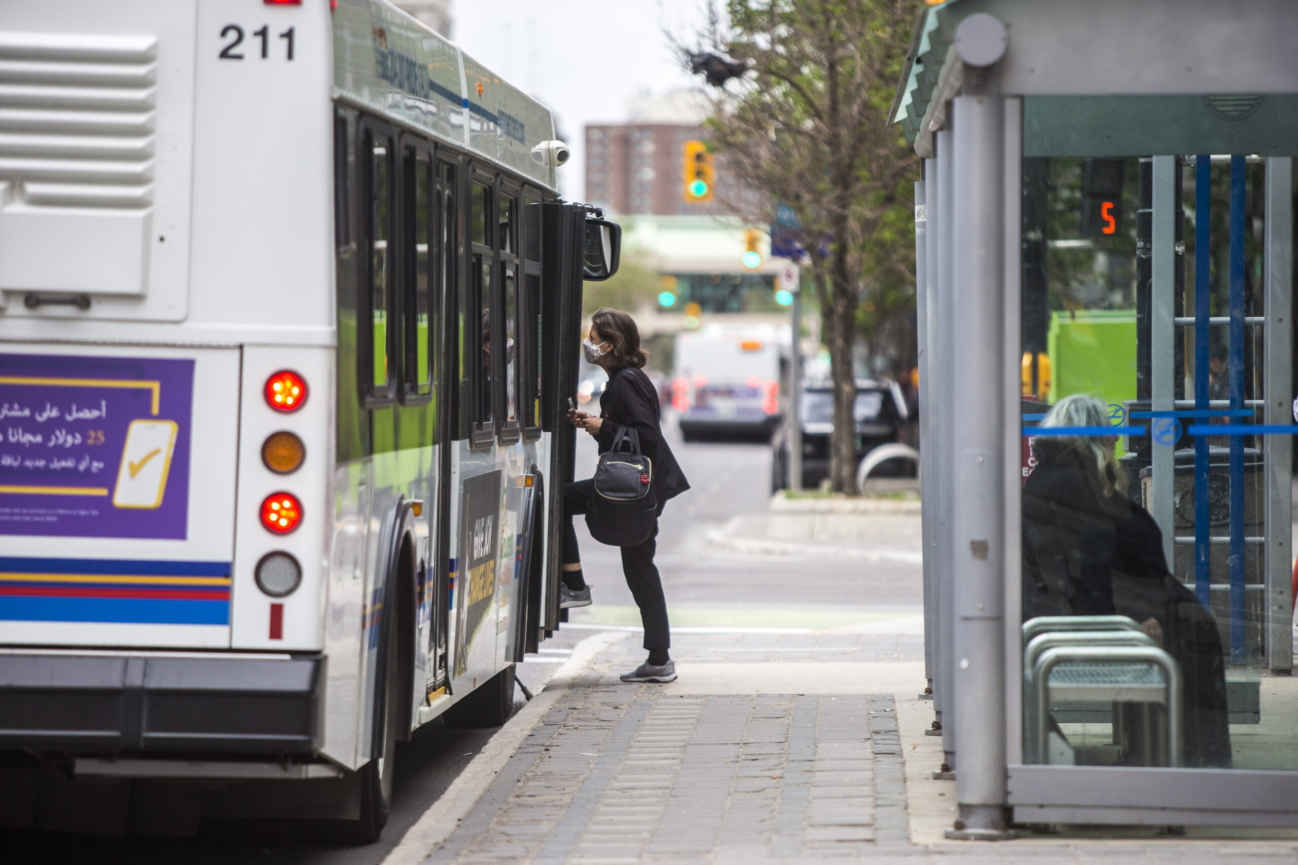 Winnipeg election: A woman in dark clothing boards a Winnipeg transit bus in front of a bus shelter
