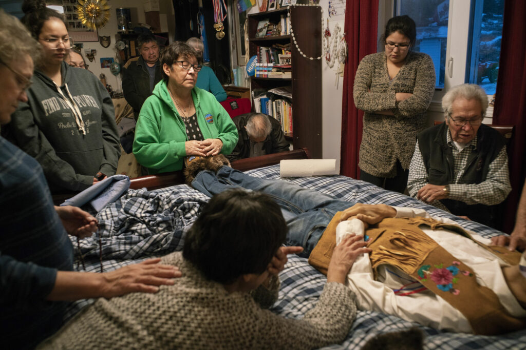 A man's body on a bed surrounded by family and friends
