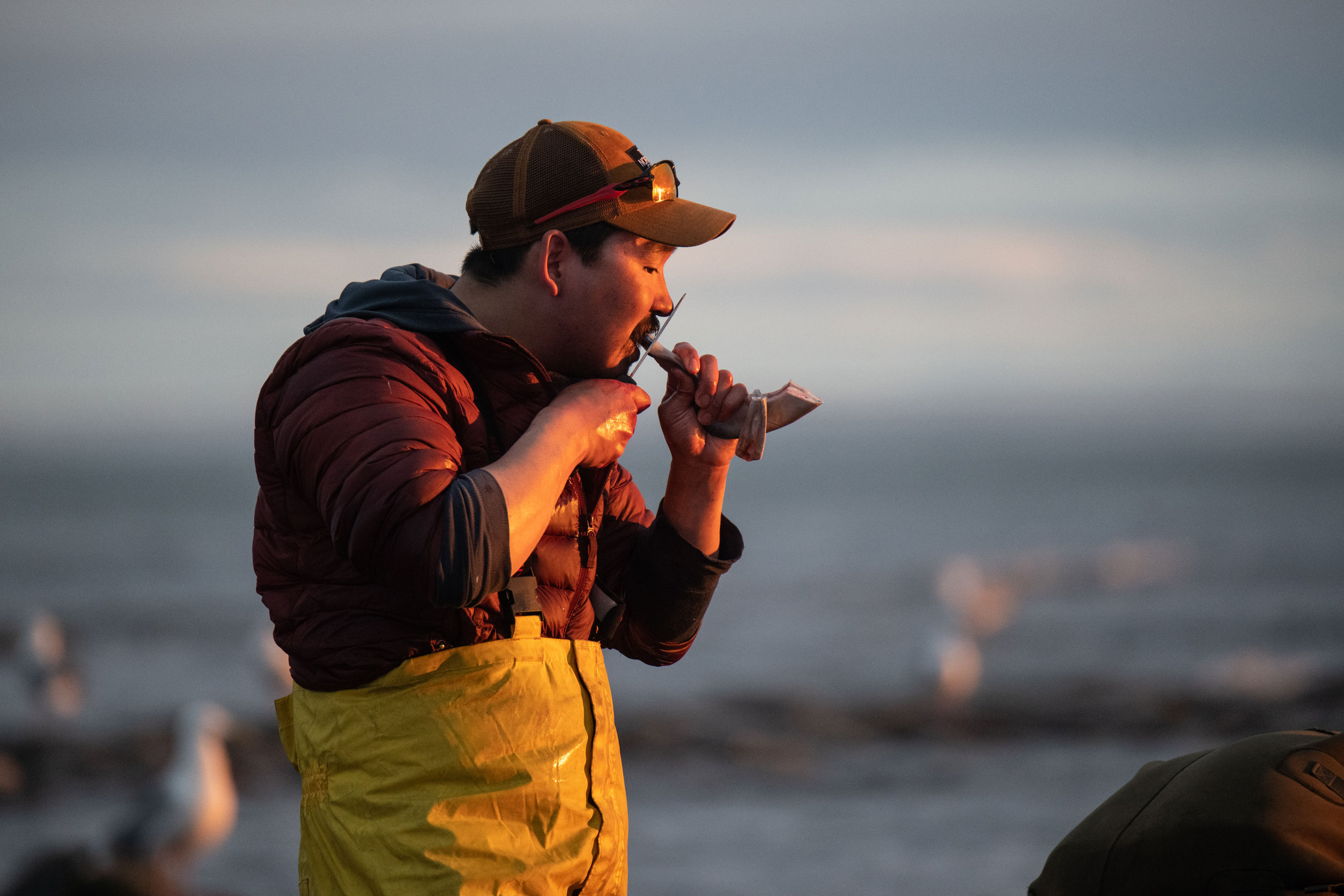 Andrew Muckpah, a Young Hunters program leader, cuts off a chunk of fresh beluga meat to chew on after a busy evening of hunting.
