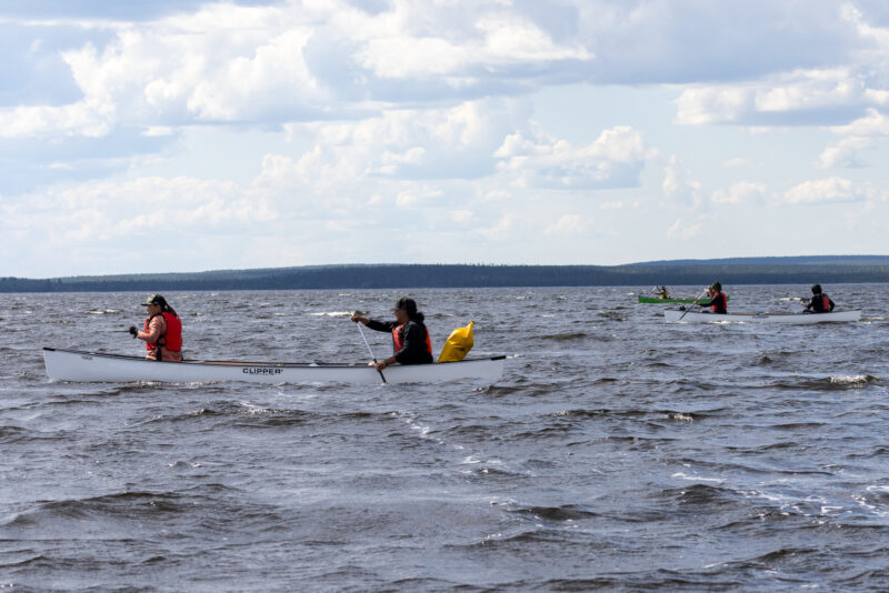 Three boats of paddlers from the Seal River Watershed Alliance Indigenous guardians program canoe through an open lake