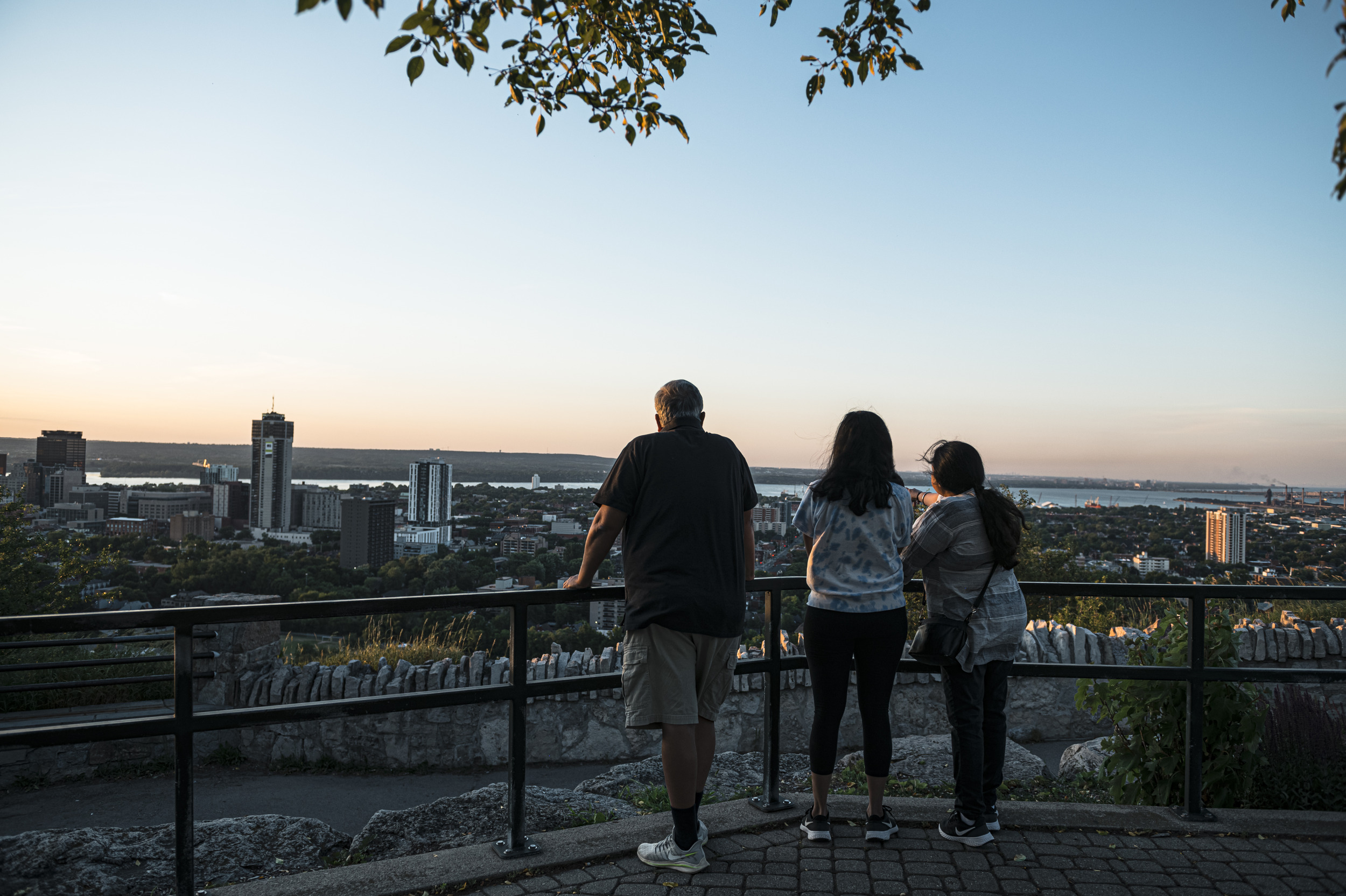 Three people with their backs turned looking at the sun setting over Hamilton, Ont.