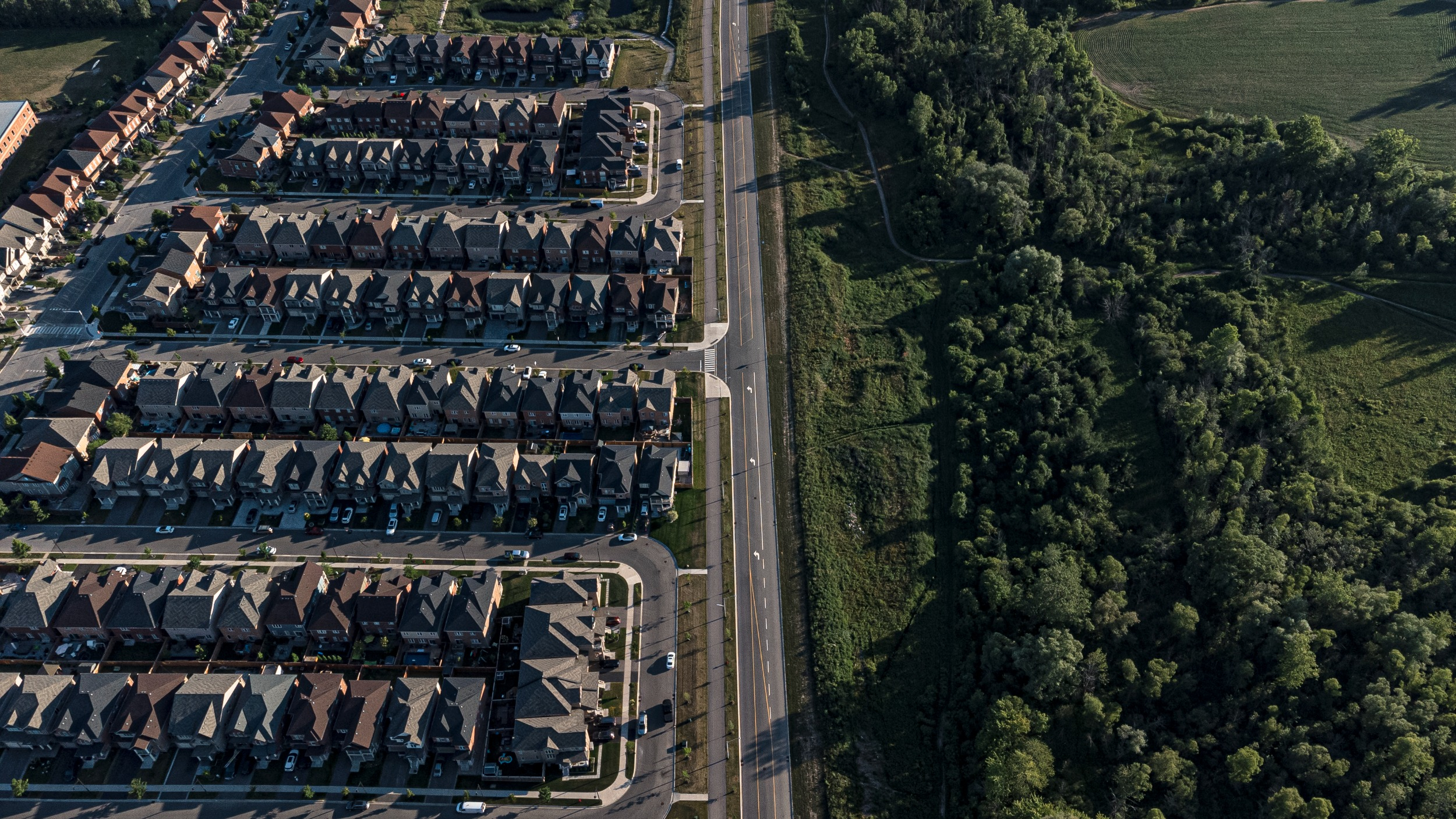 An aerial view of a road dividing a suburb from a forest and fields