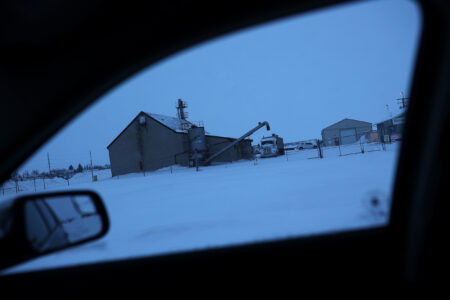 A building and auger visible out a vehicle window in the snow