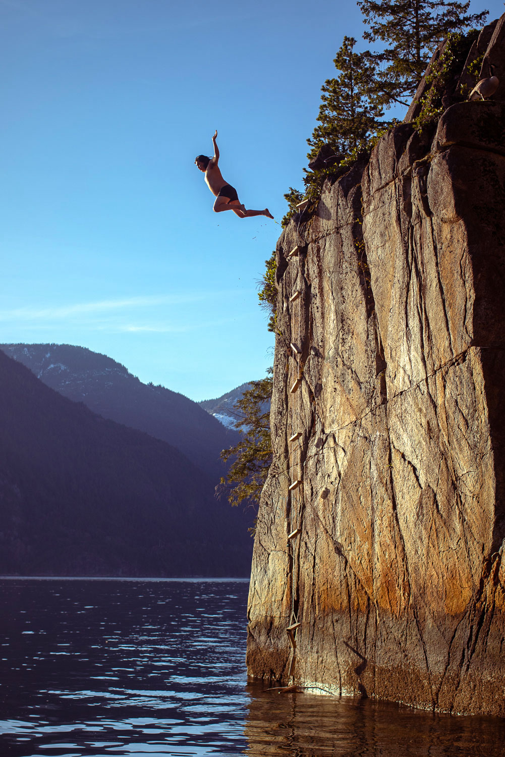 Person jumping off tall rocky cliff into ocean on sunny day