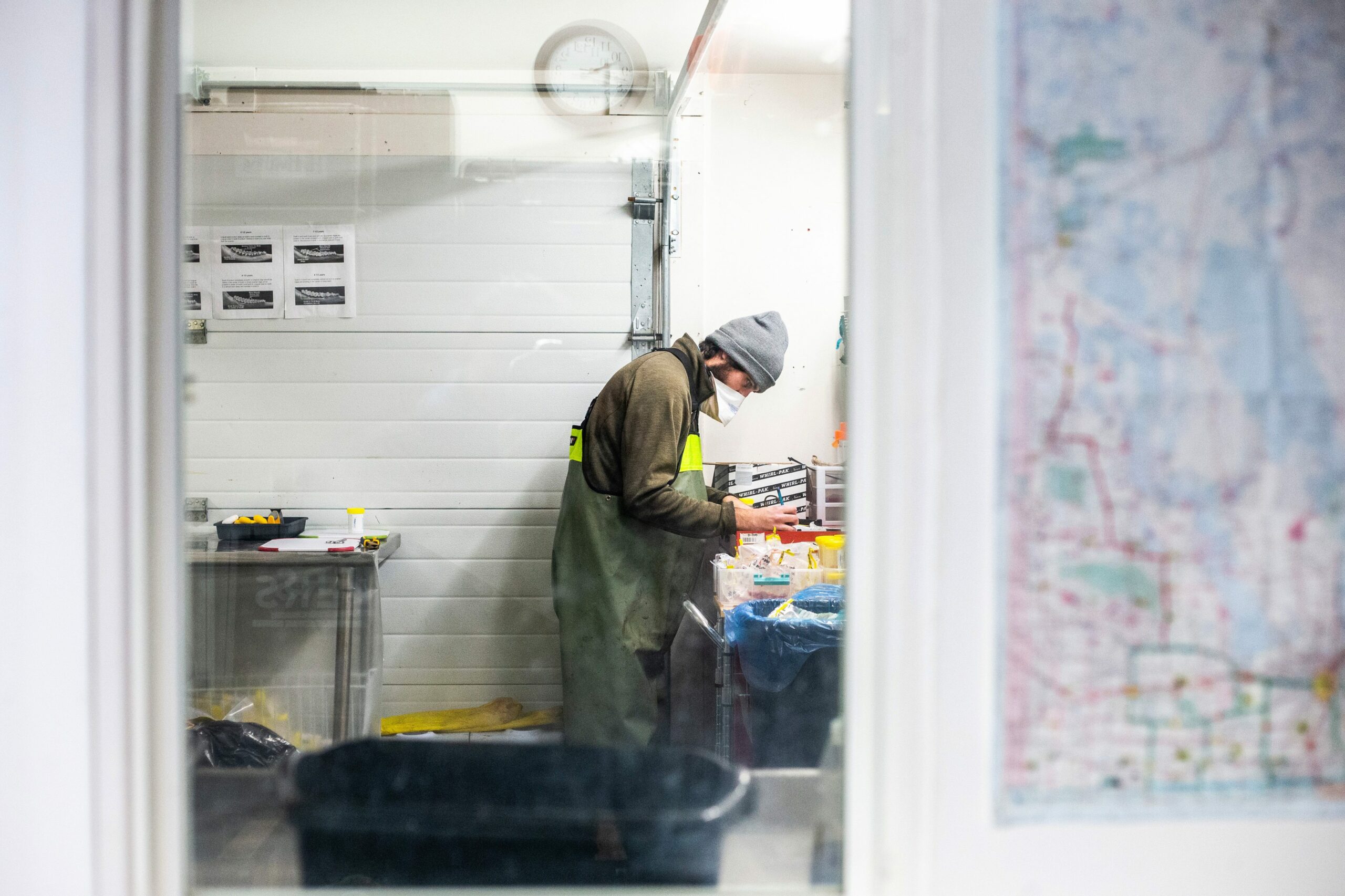 A man in green waders and a grey toque records information for a chronic wasting disease test at the wildlife health lab in Dauphin, Manitoba