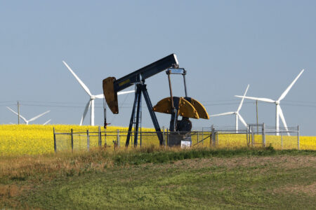 Alberta pumpjack with wind turbines in a canola field in the background