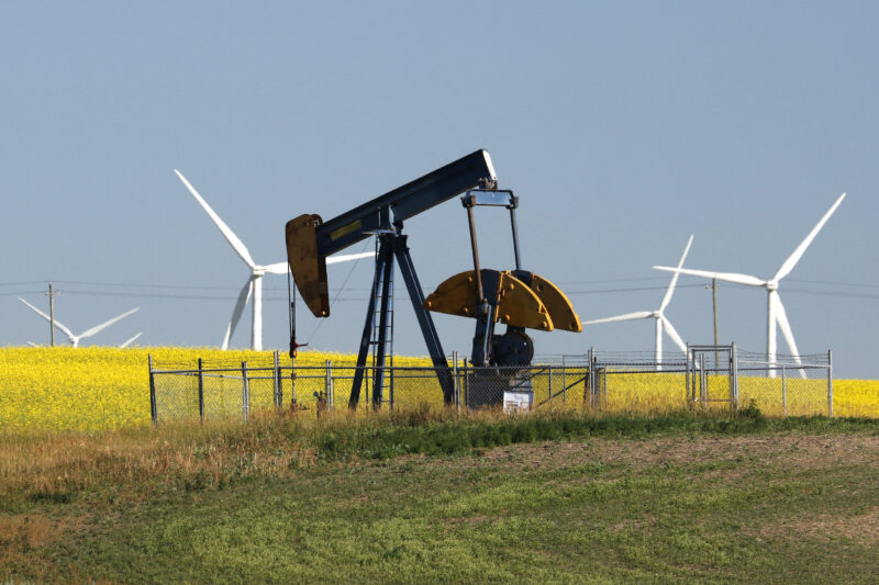 Alberta pumpjack with wind turbines in a canola field in the background