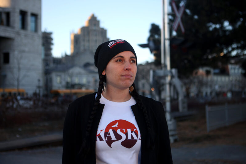 Gillian Staveley at COP15, wearing a Kaska t-shirt and a tuque that says 'Land Needs Guardians' on a sunny day in Montreal