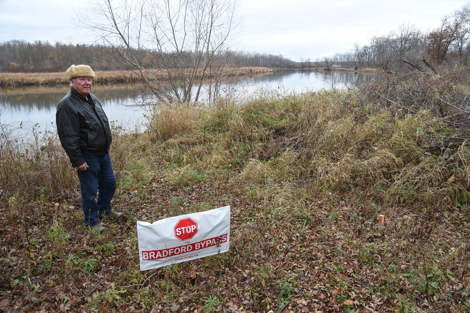 A man stands by the bank of the Holland River behind a sign that says "stop the bradford bypass"