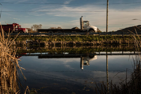 Trucks drive by a pool of water next to a highway in the Holland Marsh