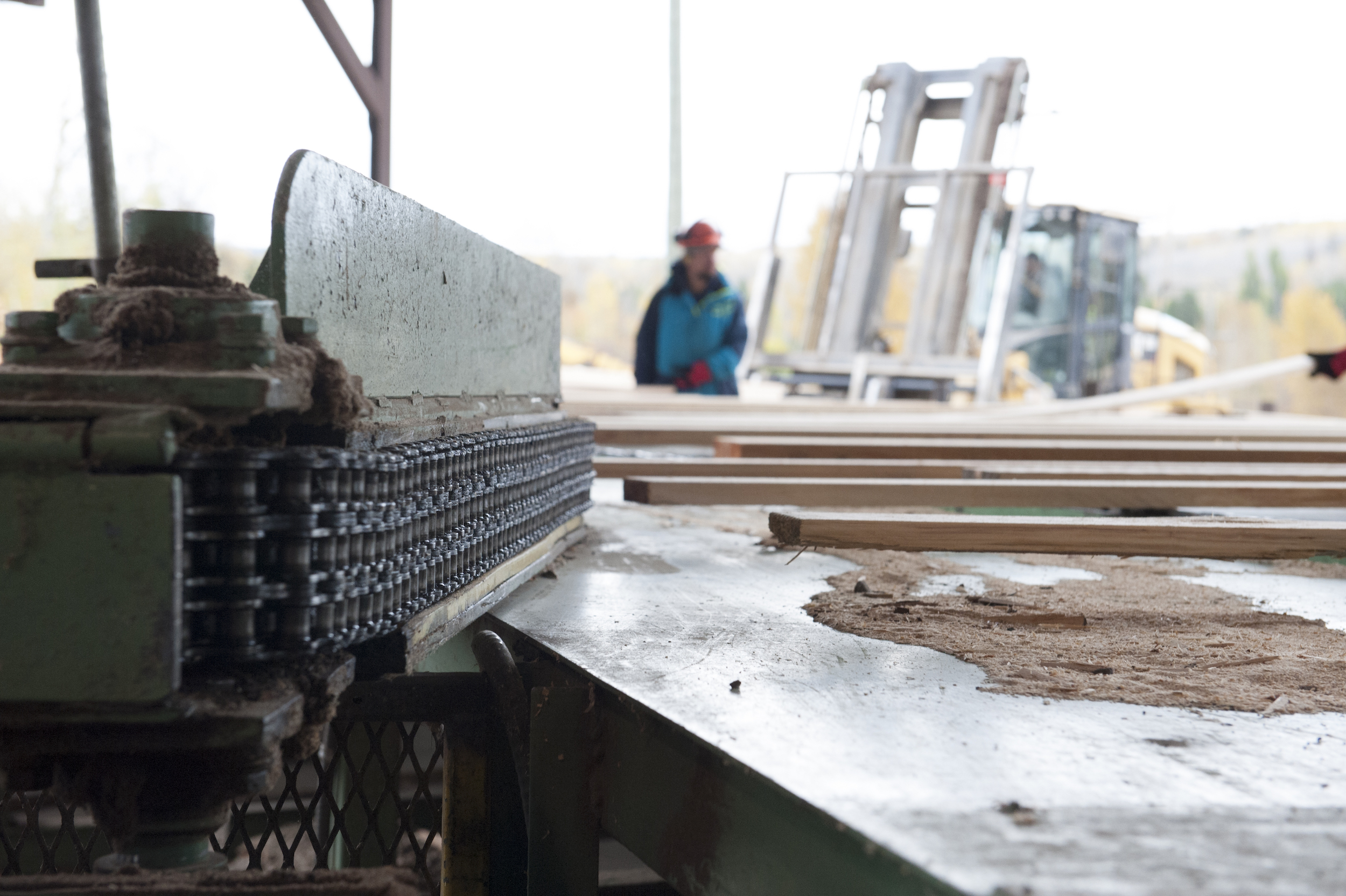 An Indigenous worker stands beside sawmill machinery In Kitwanga, B.C., with a forklift behind them