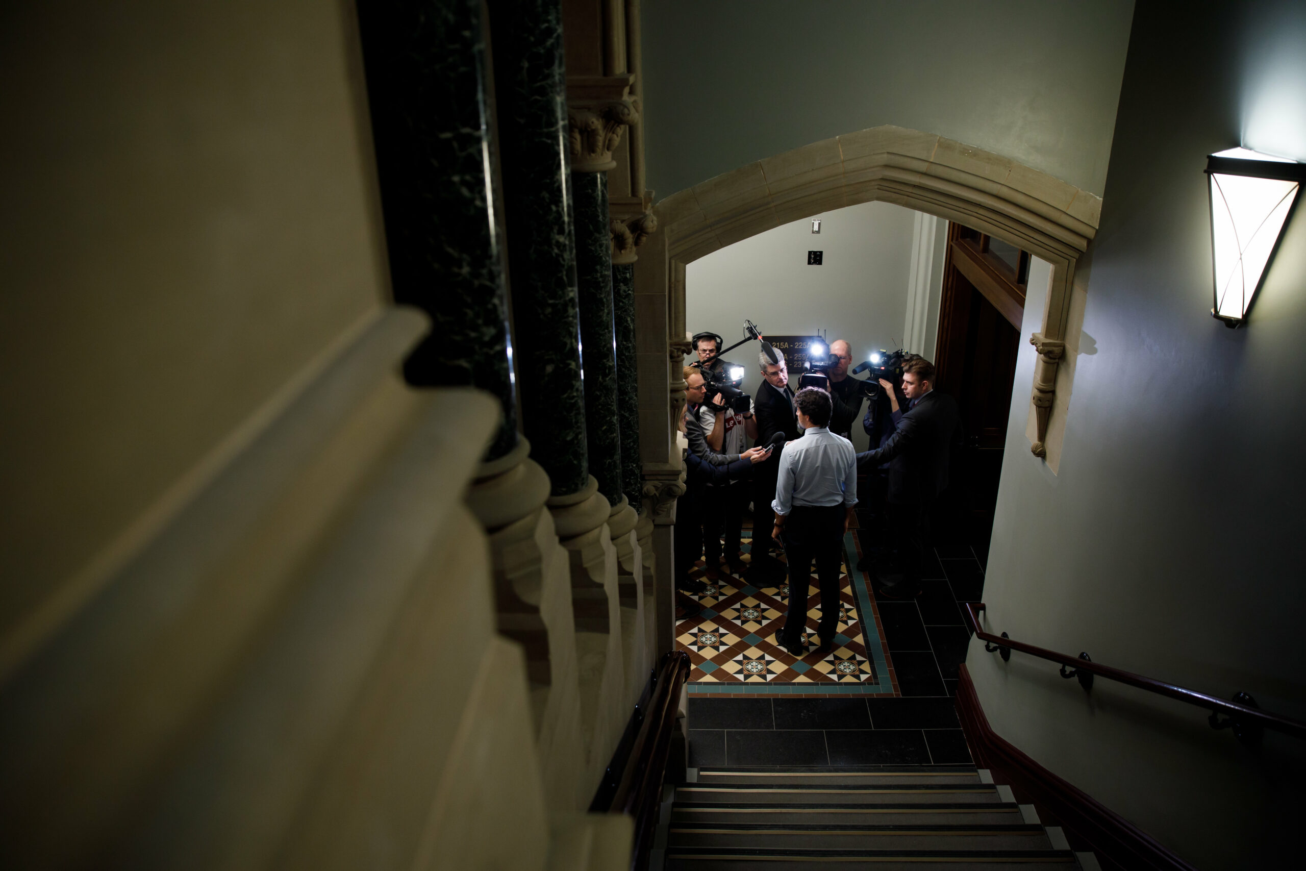 Justin Trudeau at the bottom of a staircase speaking with reporters in West Block on Parliament Hill.