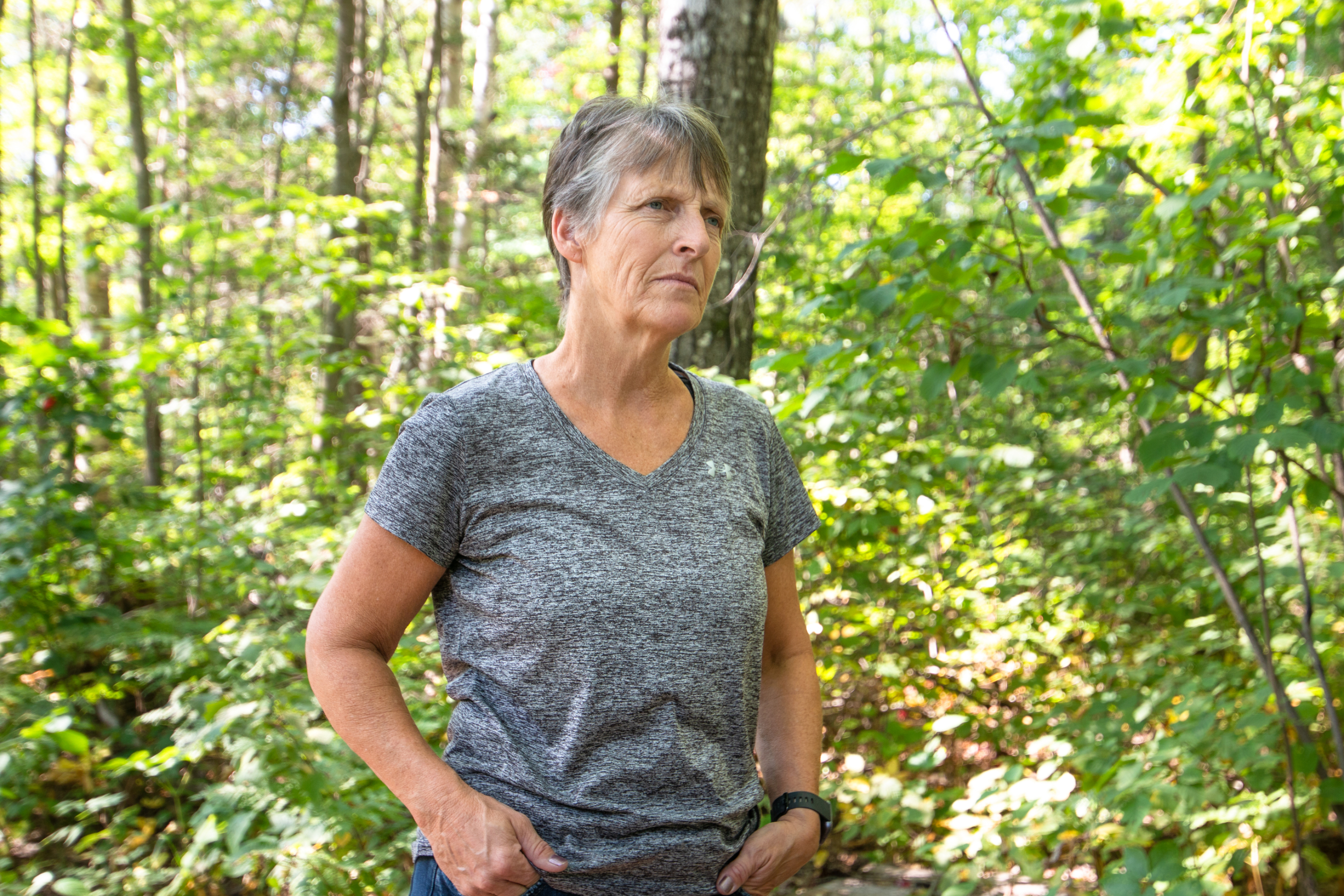 Rhonda Kirby stands with a stoic facial expression in the woods