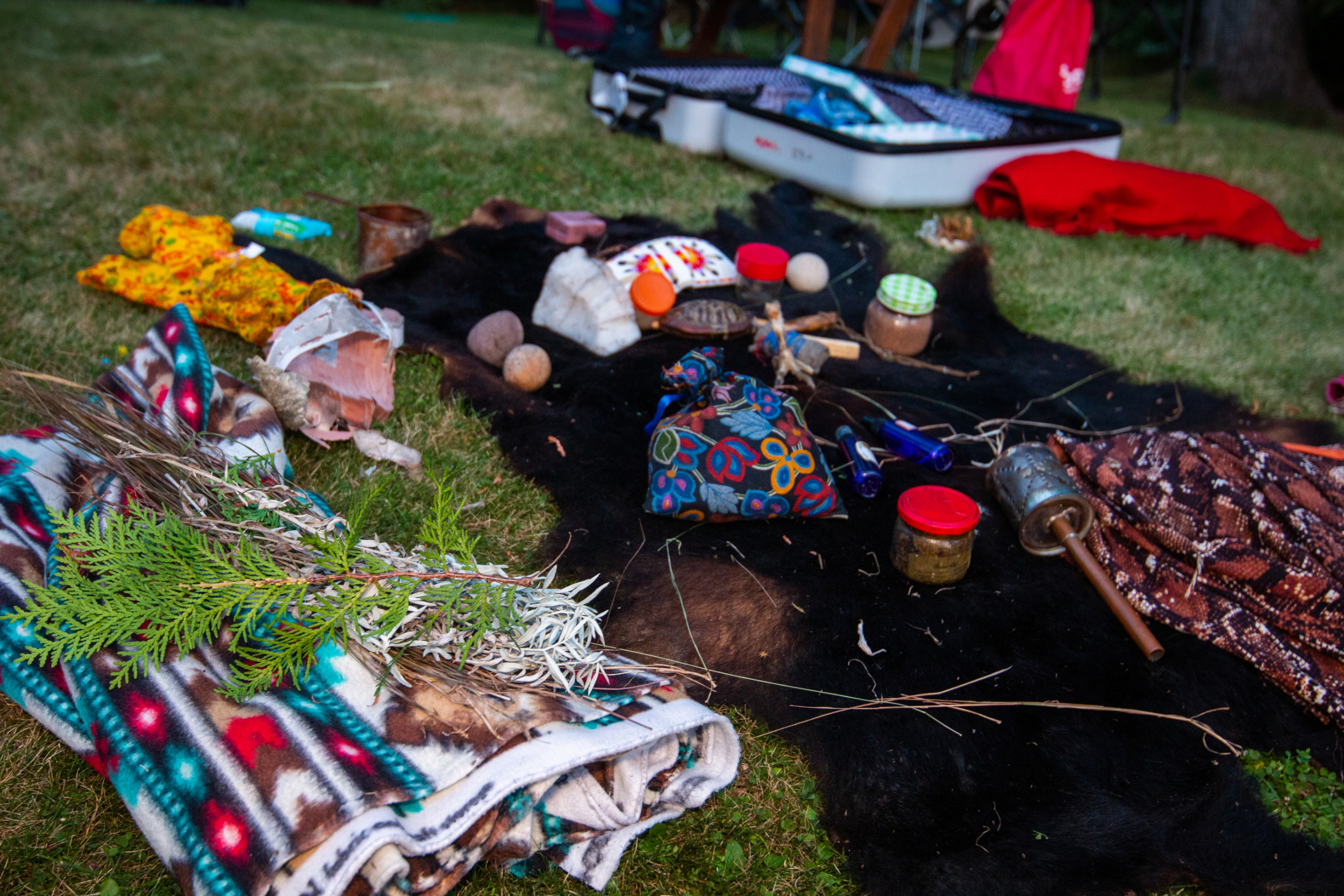 A cedar branch, blankets, a hide, a turtle shell rattle and other items spread out on grass