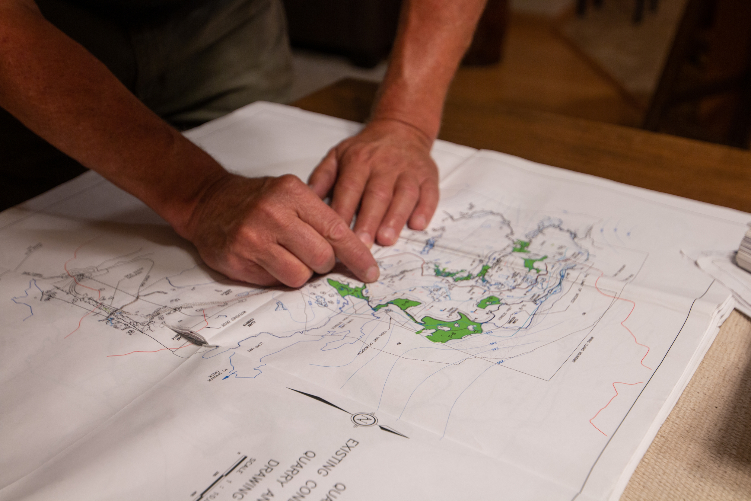 A man's hands point to a quarry on a map spread out on a table