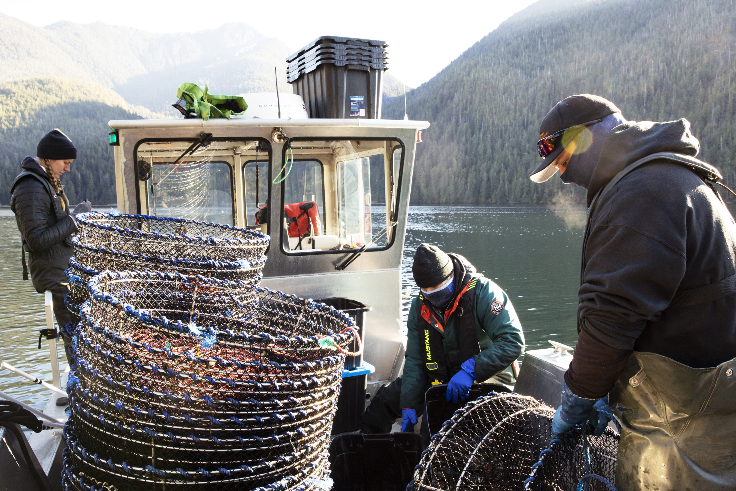 Coastal Restoration Society biologist Janessa Dornstauder stands on the left side of a boat recording the number of European green crabs collected from a set of traps in Bedwell Sound, near Tofino, British Columbia. Prawn traps are piled in the foreground