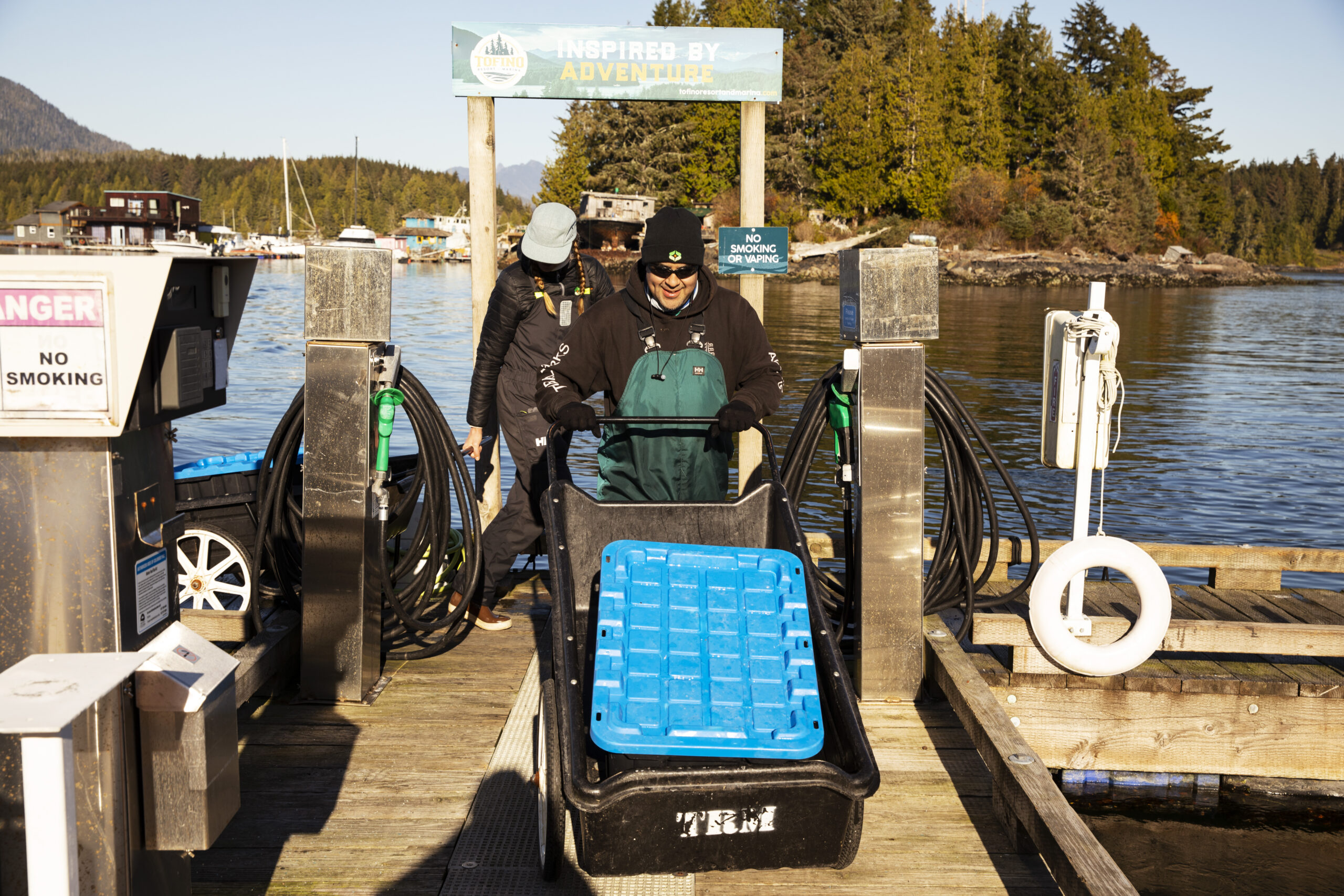 Coastal Restoration Society biologist Janessa Dornstauder and technician Joe Louie move a tote with a blue lid full of the European green crabs they collected in Bedwell Sound up the dock. The crabs are headed to the freezer.