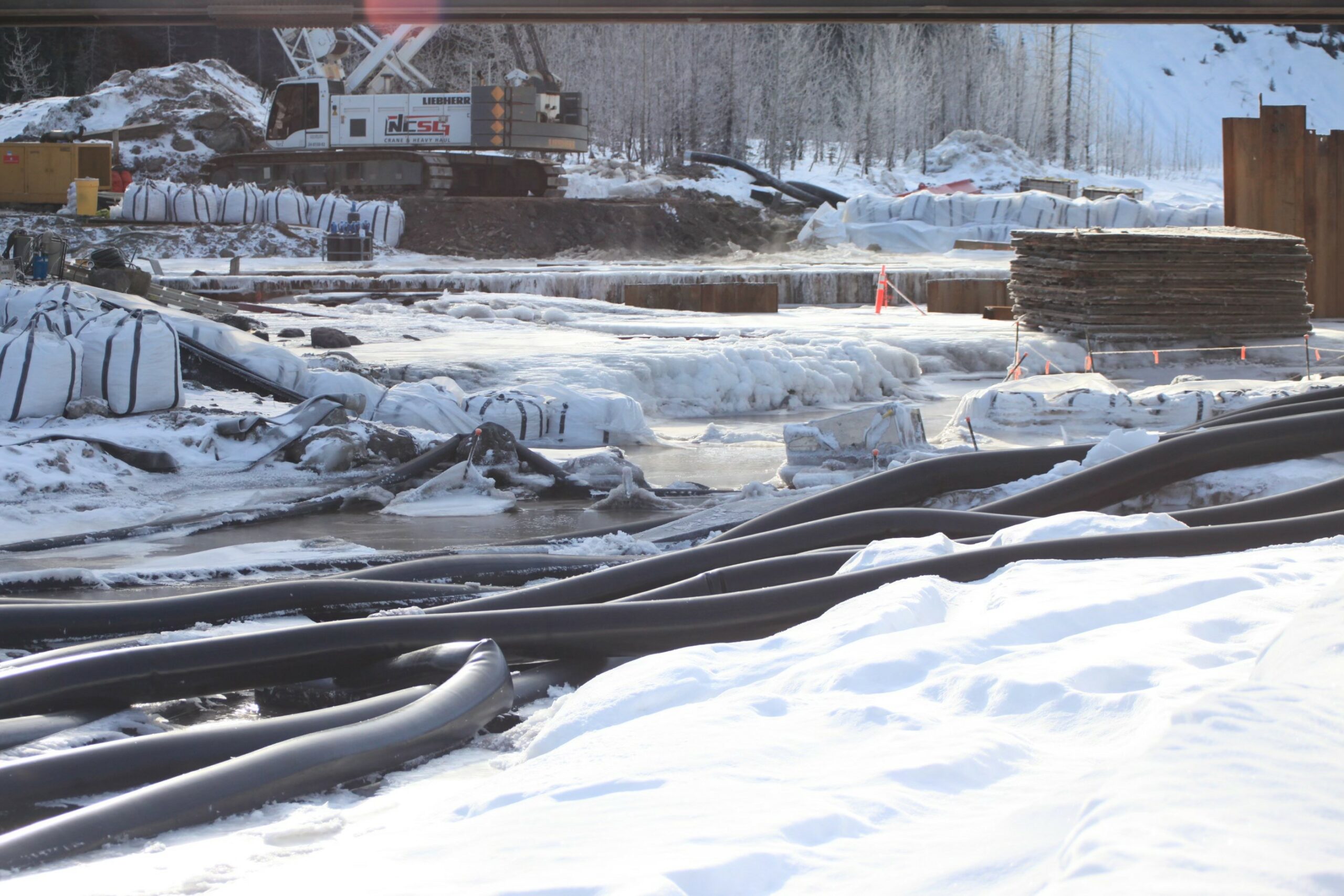 Ice and water at a Coastal GasLink construction site, snake-like pipes in the foreground