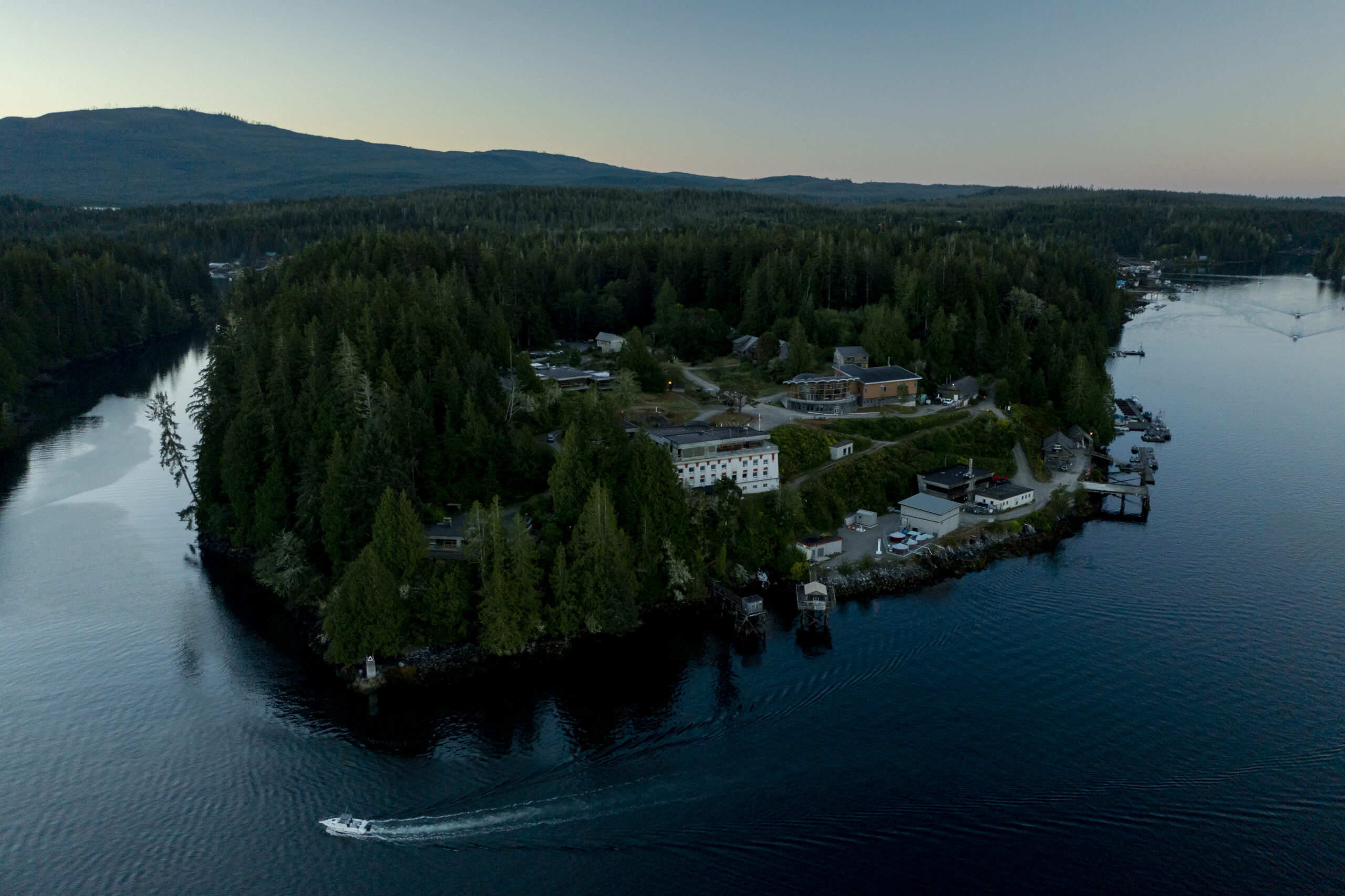 An early morning aerial shot of the Bamfield Marine Sciences Centre surrounded by forest. Recreational fishing boats can be seen heading out the inlet.