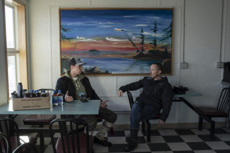 Reporter Drew Anderson talking with Calvin Waquan, a member of the Mikisew Cree First Nation. Waquan has a box of bottled water next to him, with oil mixed in the bottles.