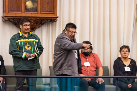 Chris Moonias stands at a railing and points downward as others look on