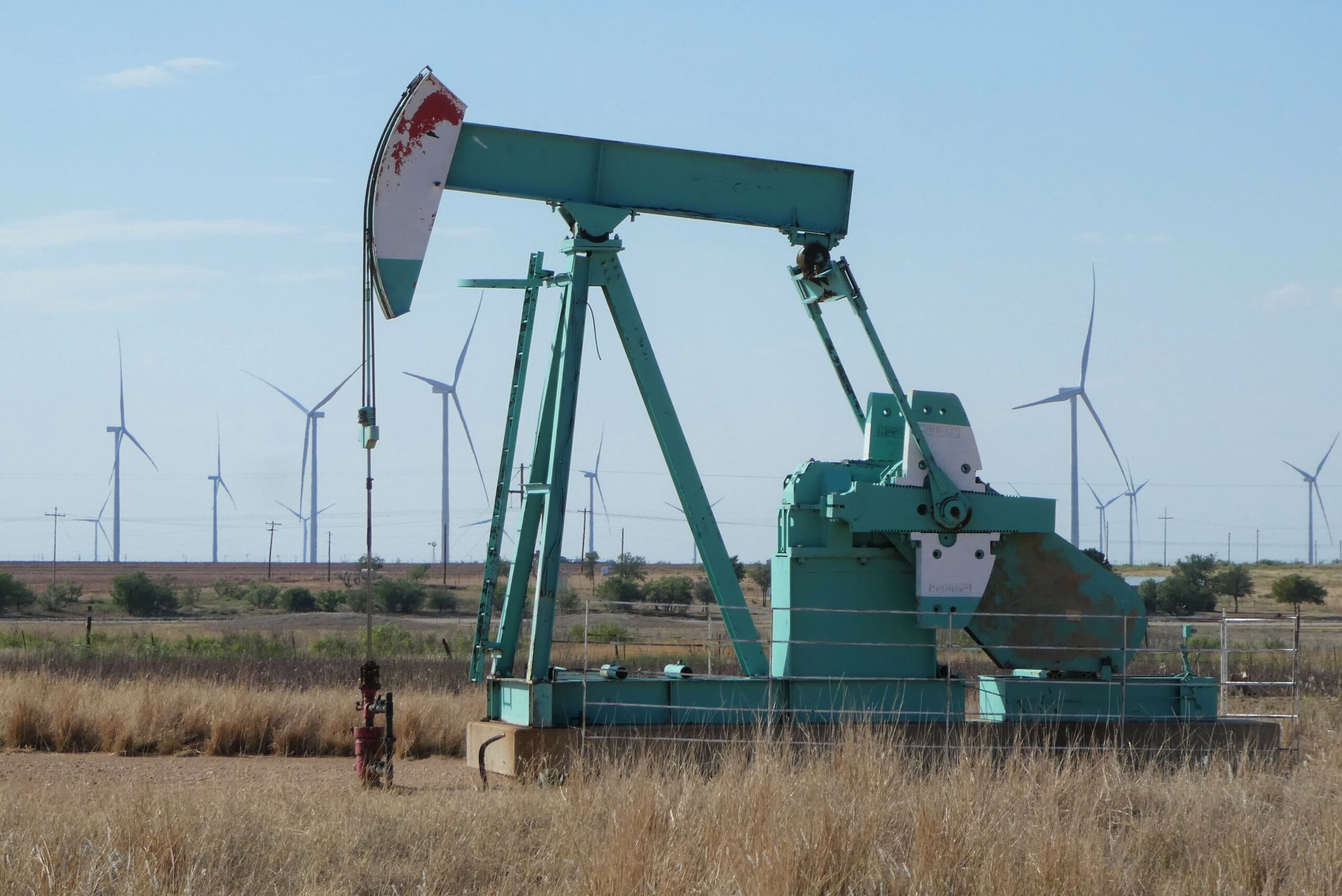 Oil pumpjack in the foreground with wind turbines in the background in a field in Texas.