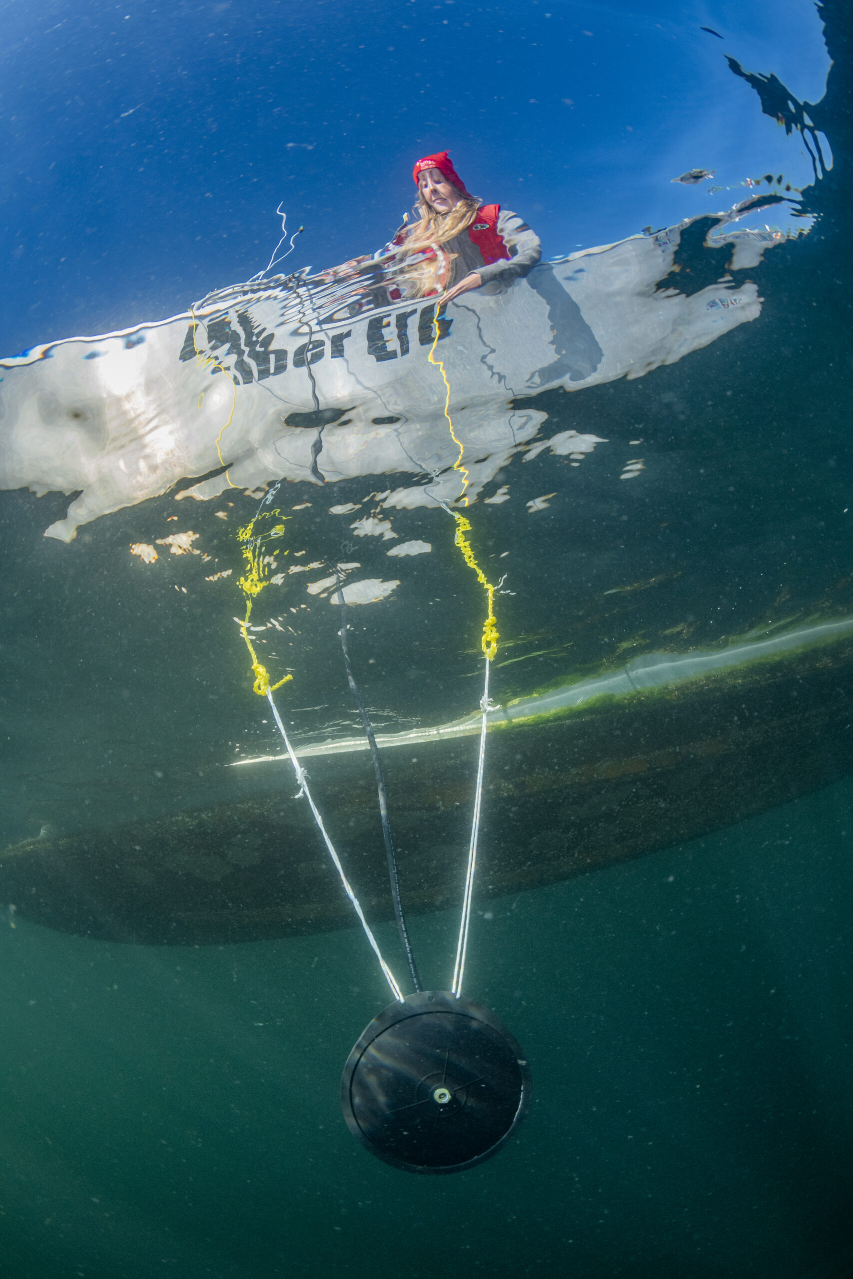an underwater photo of a disc-shaped speaker suspended from a research boat