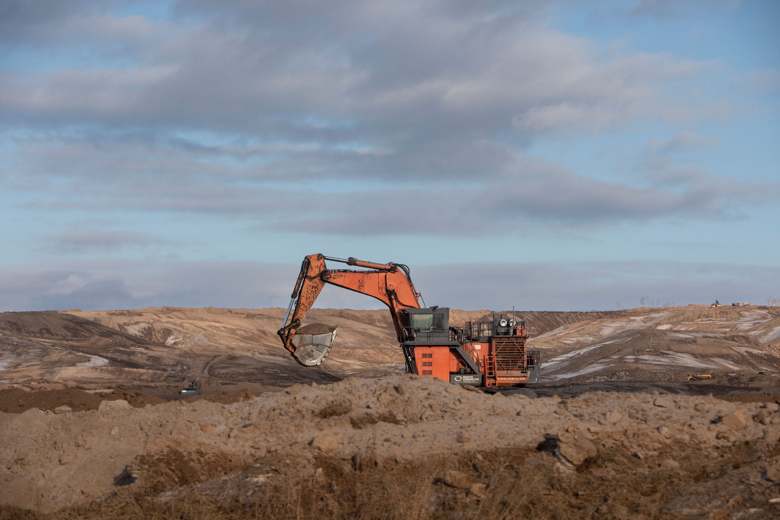 An orange excavator digs into brown surroundings at the Alberta oilsands.
