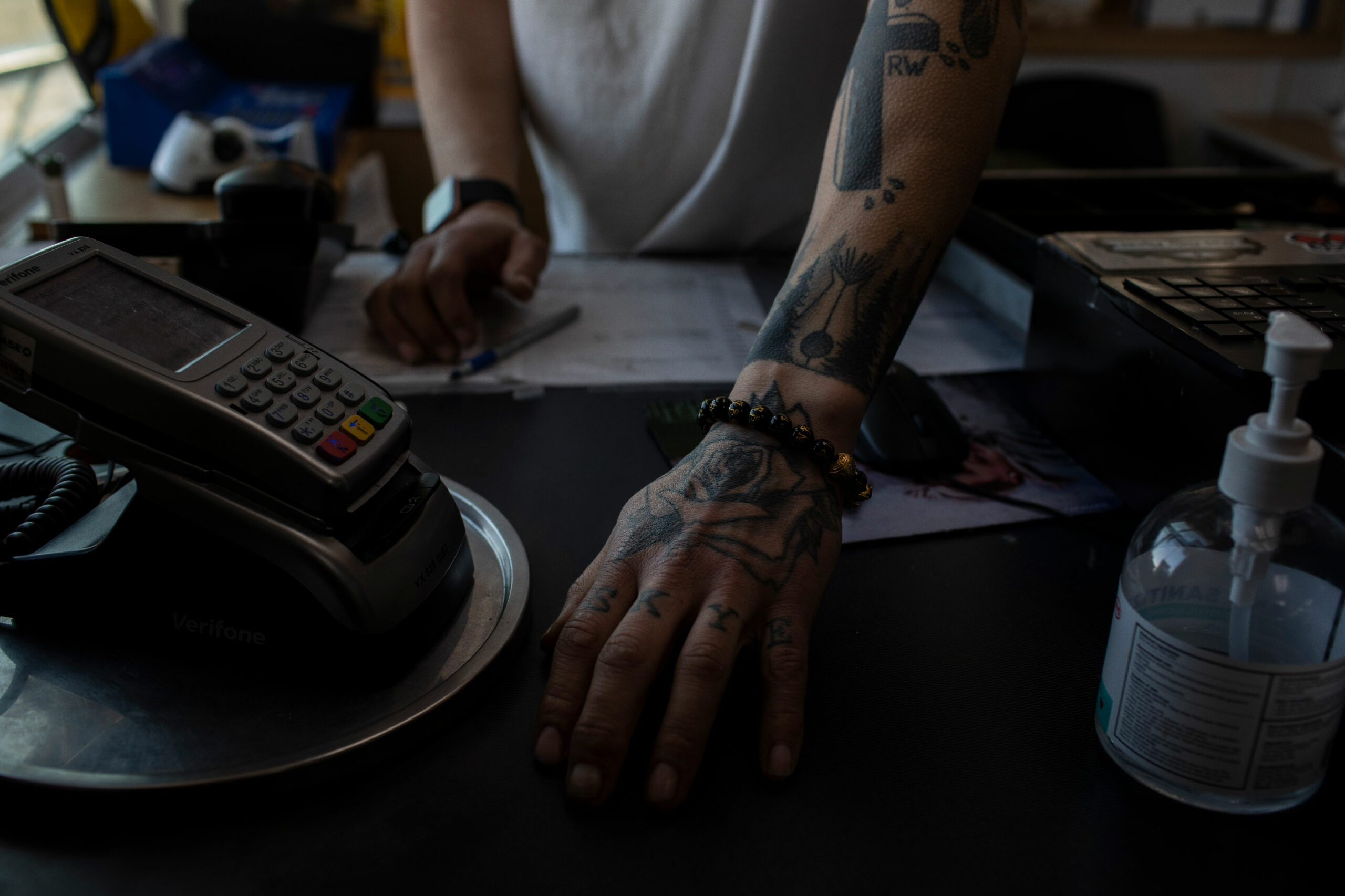 Detailed photo of the tattooed arms of a man behind a cash register in a convenience store in Fort Chipewyan.