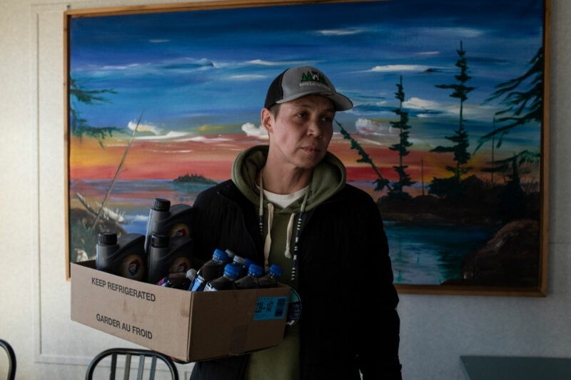 Calvin Waquan at his family's store and gas station in Fort Chipewyan, Alta., holding a box of water bottles with oil mixed in them.