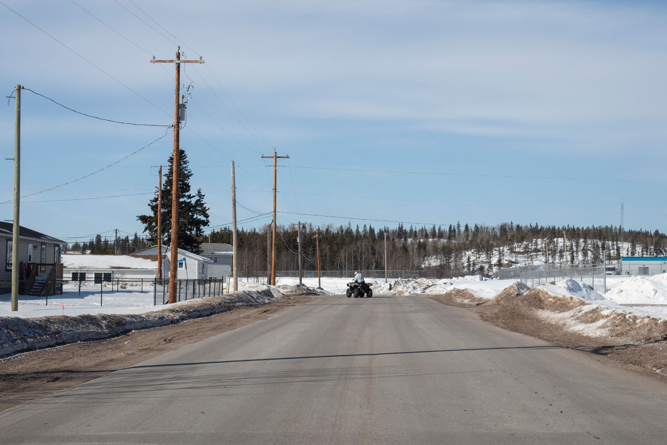 A person drives an ATV along a road in Fort Chipewyan, Alta.