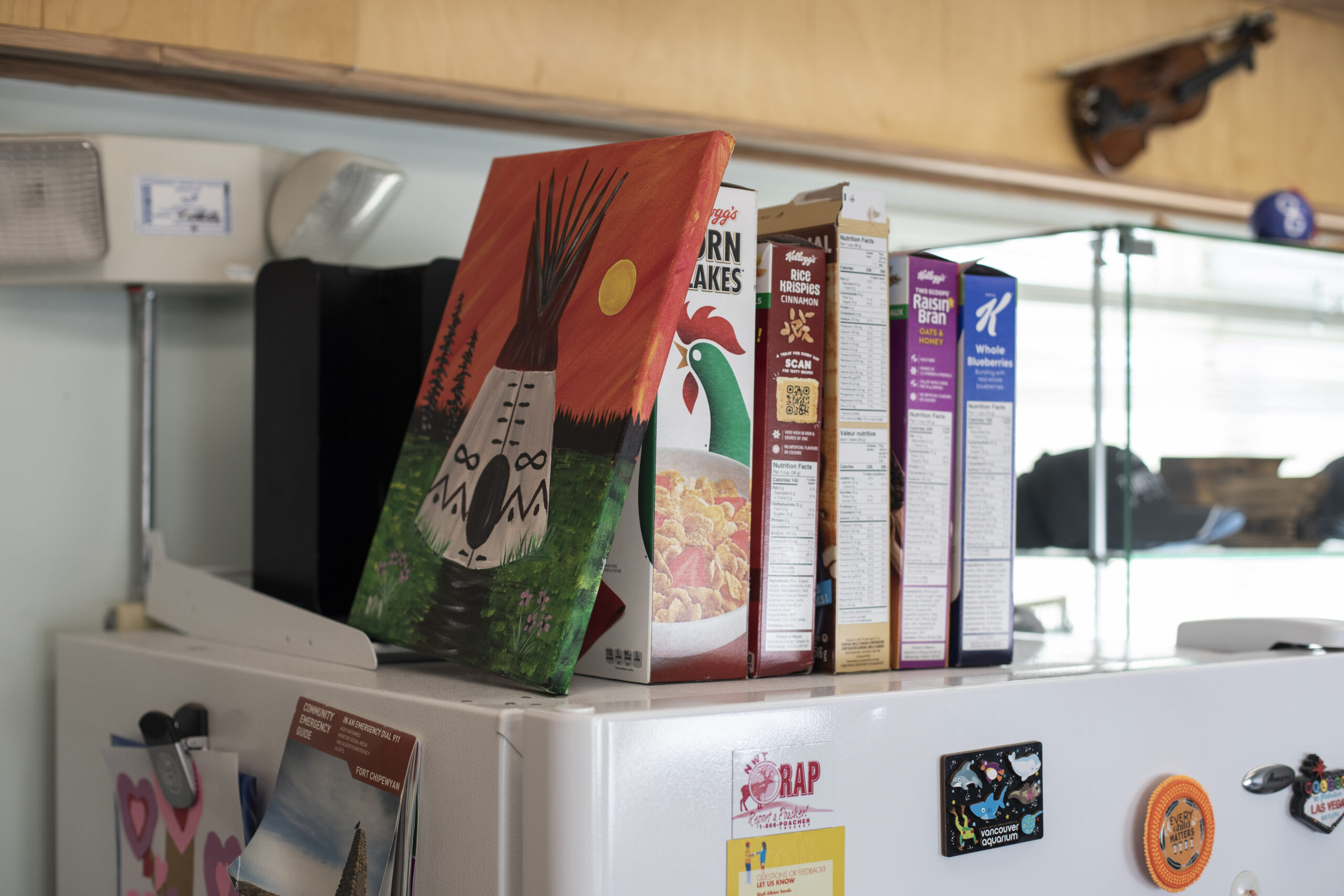 Cereal boxes are stacked on the top of a white fridge.