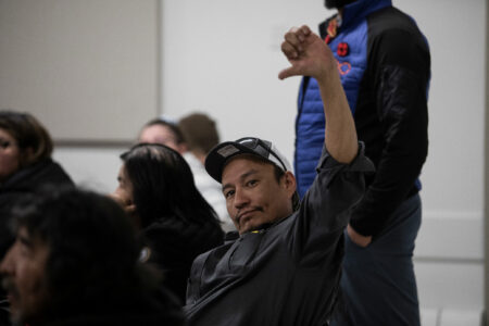 A man in a crowd gives a thumbs-down sign at a meeting with Imperial Oil to talk about leaking tailings ponds in Fort Chipewyan, Alta.