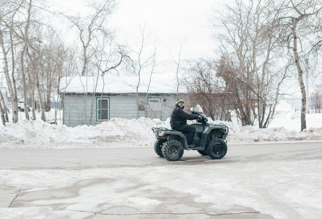 A man rides an ATV down a street, lightly covered with packed snow.