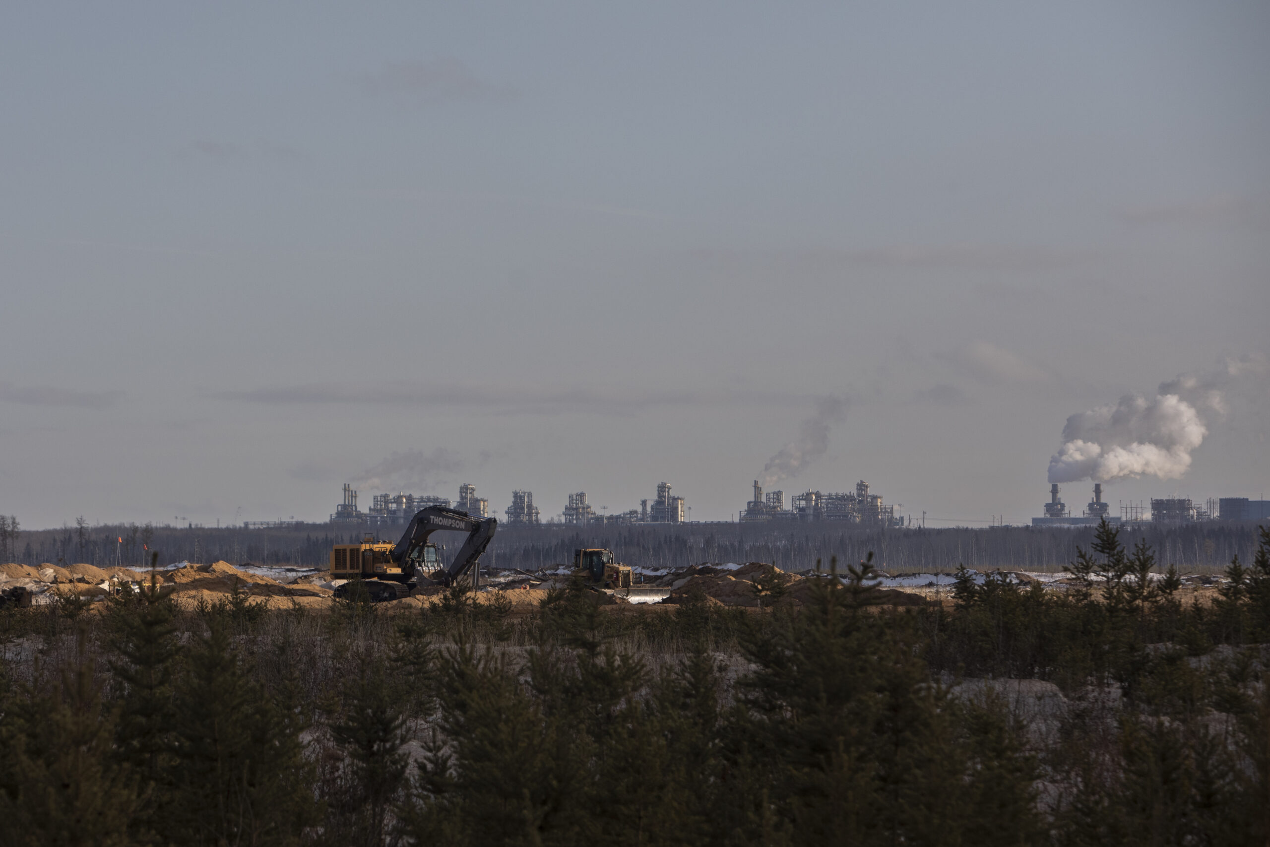 Excavators in the foreground at Suncor's Fort Hills oilsands mine with a refinery visible on the horizon