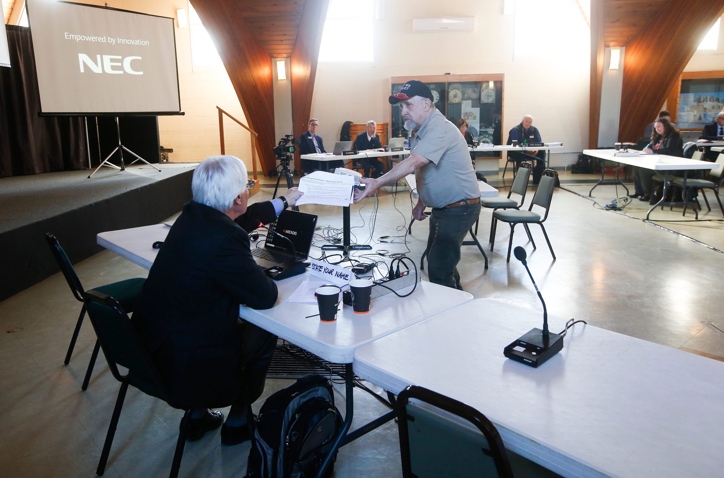 A southeastern Manitoba resident wearing a ball cap and short-sleeved shirt hands a document to a geological scientist during a clean environment commission hearing in Steinbach, Manitoba over a proposed silica sand mine