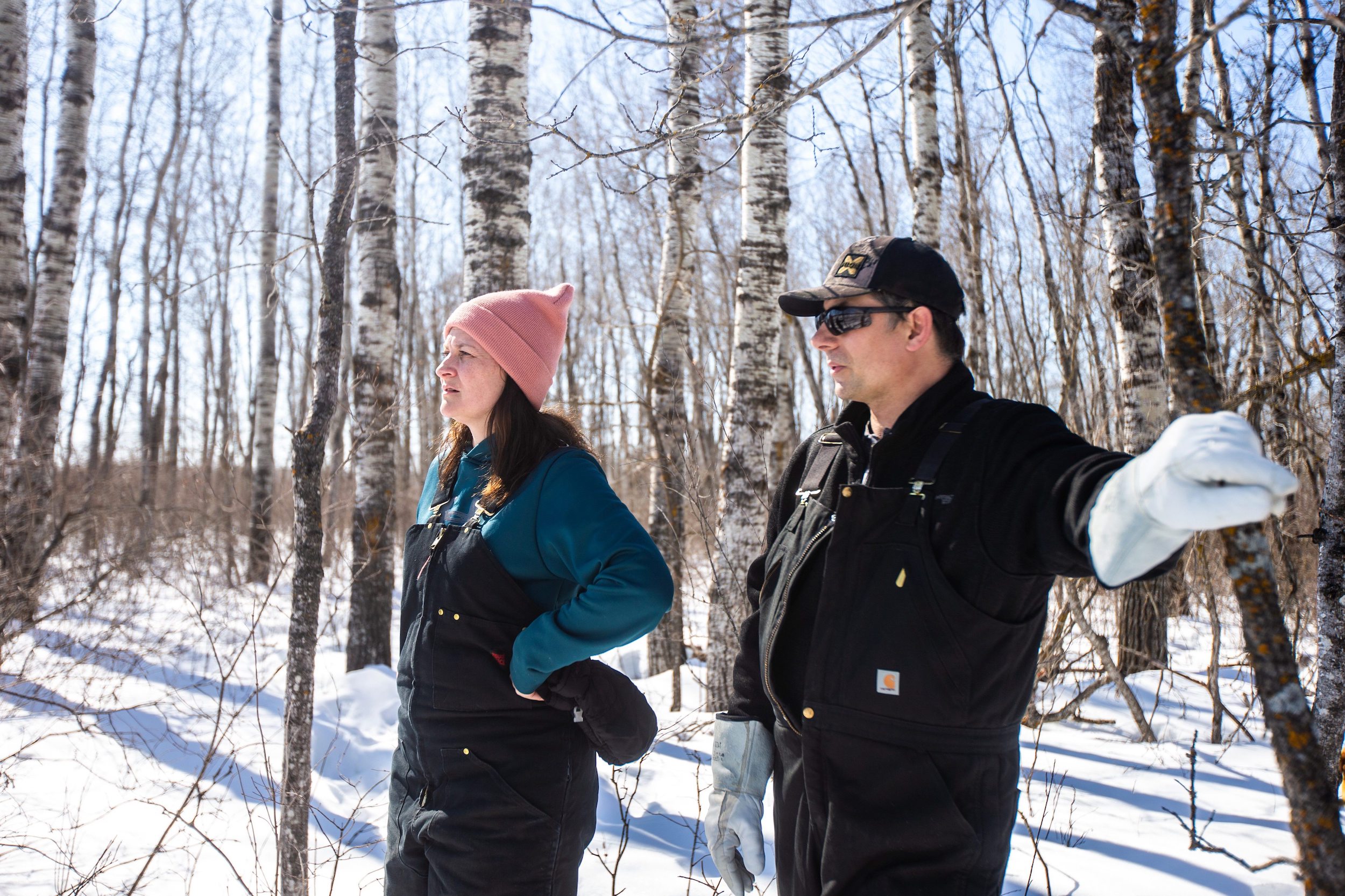Josh and Georgina Mustard stand in the snowy woods at the back of their property near Vivian, Manitoba. Josh leans against a tree as they both look toward the clearing where Sio Silica plans to build a sand processing facility