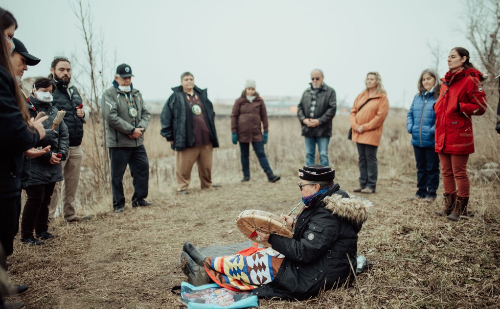 Photos of Caldwell First Nation ceremonies to mark the return of land to Indigenous stewardship. A woman sitting on the ground with a drum, others standing around her in a circle.