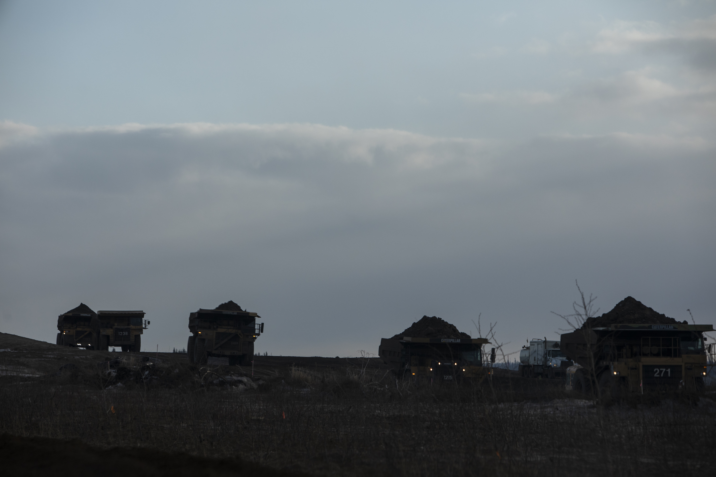 Silhouetted loaded heavy hauler trucks in Suncor's Fort Hills oilsands mine