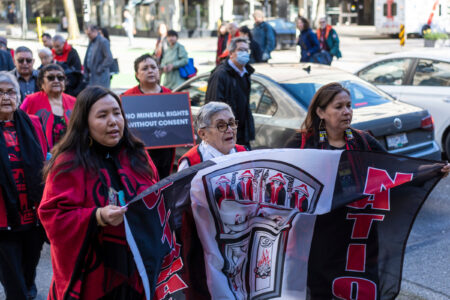 A group of people hold a flag that reads Gitxaała Nation and a sign that says "no mineral rights without consent" as they walk to the B.C. Supreme Court in Vancouver.