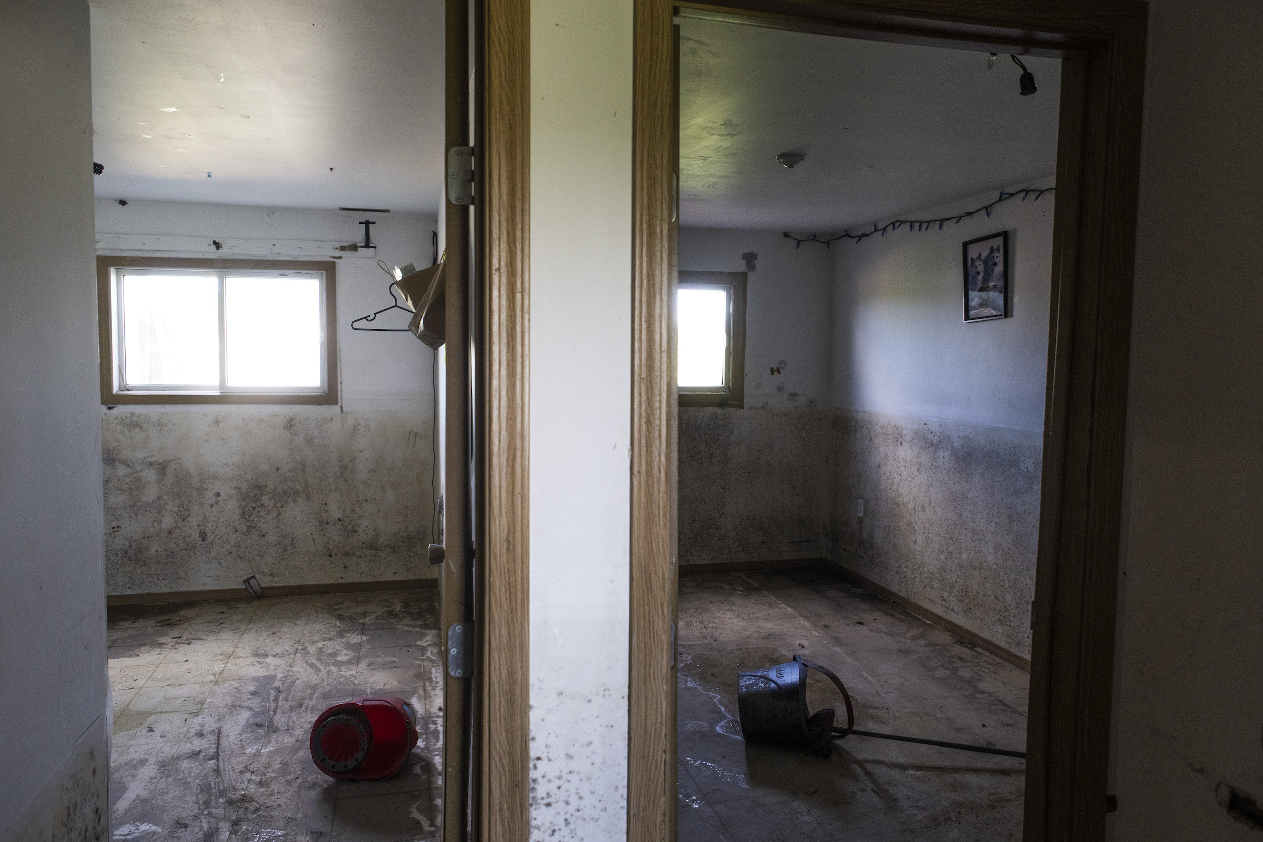 Two empty rooms, separated by a wall in the centre of the frame, with mold damage on the walls as high as the windowsills and overturned mop buckets on the floor at a home in Peguis First Nation