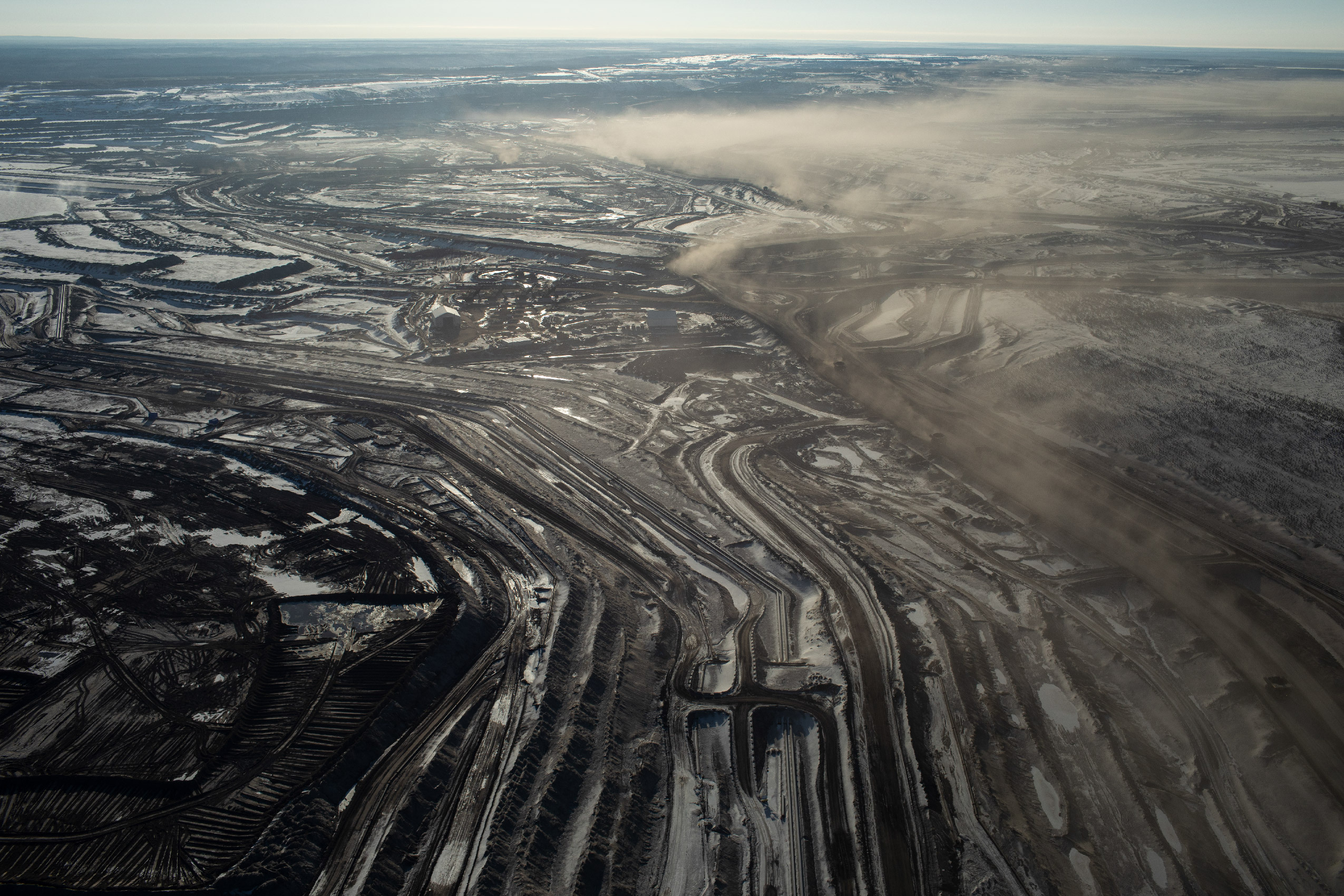 Dark muddy brown surface in the Alberta oilsands seen from the air cris-crossed with offroad tracks.