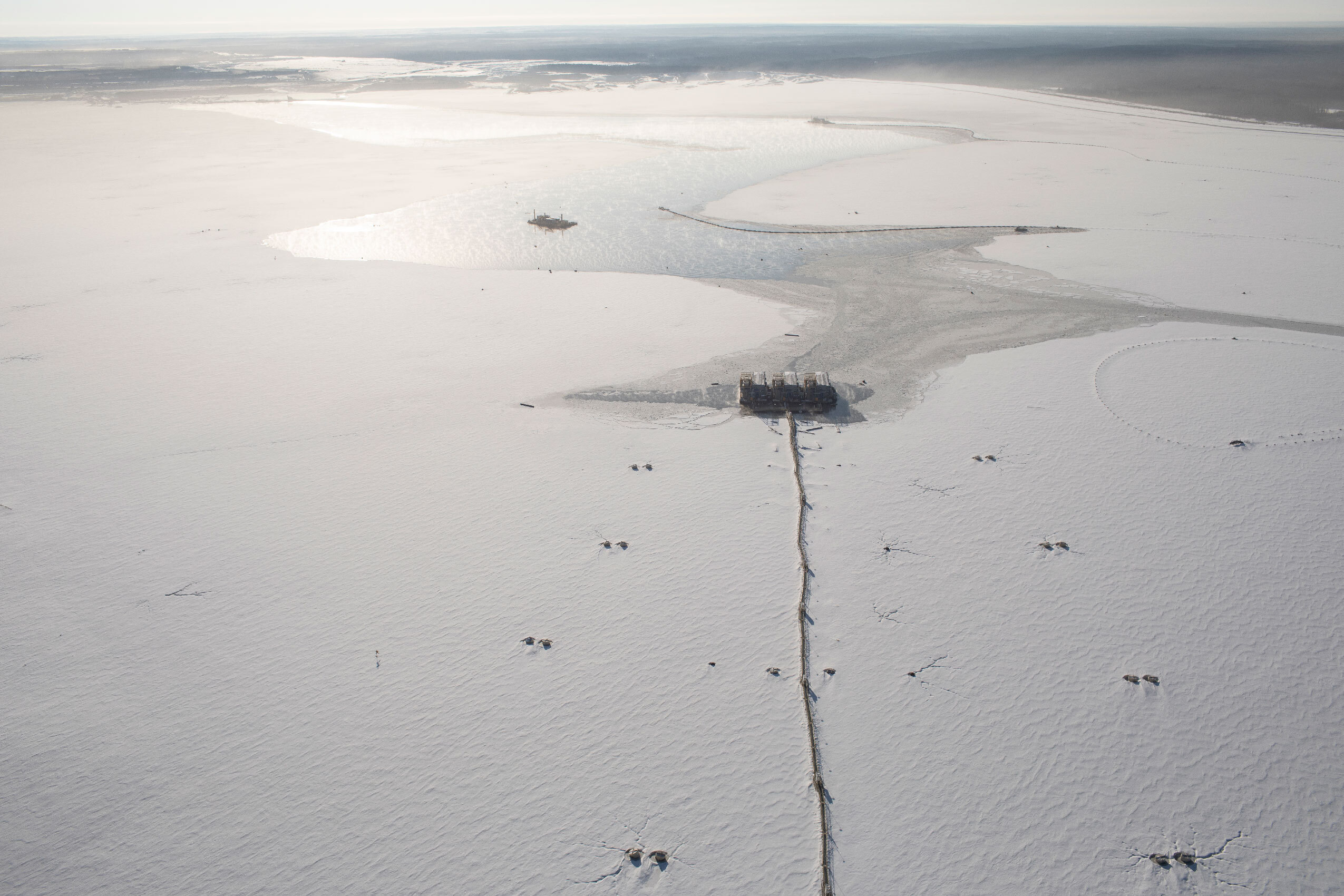 Overhead view of a frozen lake in Alberta with a pipeline running up the middle to a spot in the centre.